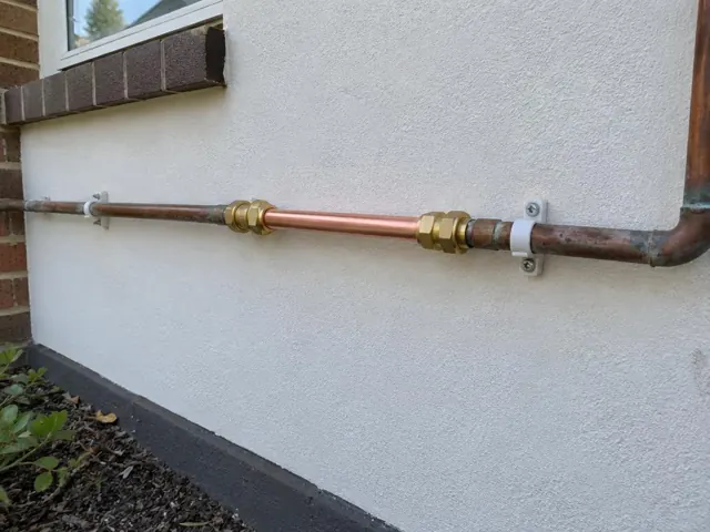 Copper water pipe repair on a rendered exterior wall with brackets in Weston