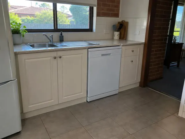 Kitchen with a white dishwasher under a stone benchtop beside a sink and cream cabinets in Abermain