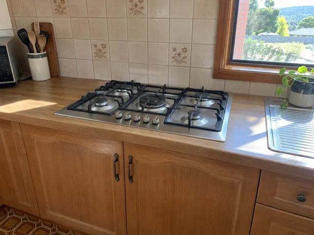 Stainless gas cooktop set into a timber benchtop with tiled splashback and window in Sawyers Gully